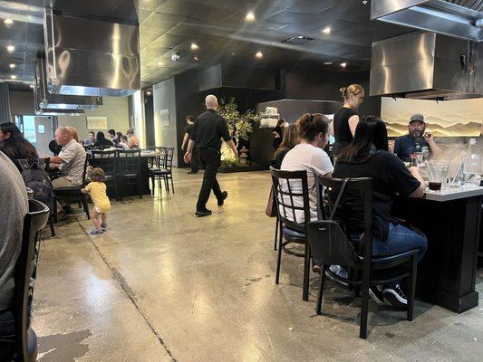 Patrons are squished together around a table even though there's tons of empty floor space