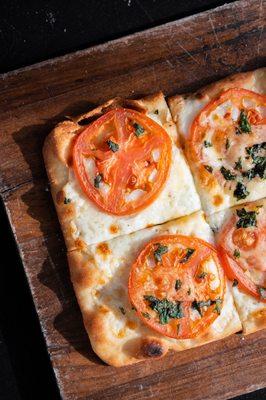 Close up image of flatbread pizza with tomatoes, cheese, and herbs