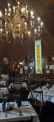 The dining room of The Gift Horse with stained glass window and chandelier.