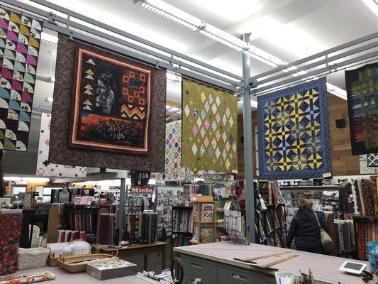 Lots of quilt samples (patterns all available to purchase) hanging above the center check out counter.