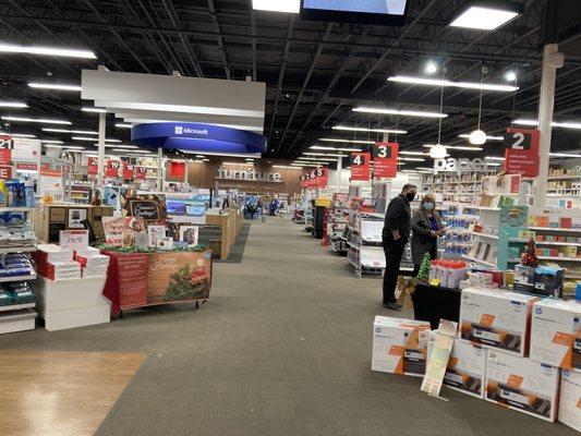 Displays of merchandise and several aisles of office and home products with a customer receiving assistance.