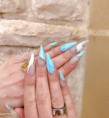 Swirling sky blue and white marble design on stiletto nails, edged with gold. #MarbleNails #BlueWhiteGold