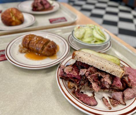 Pastrami on rye, cucumber salad, kishka. Beef knish on the background.