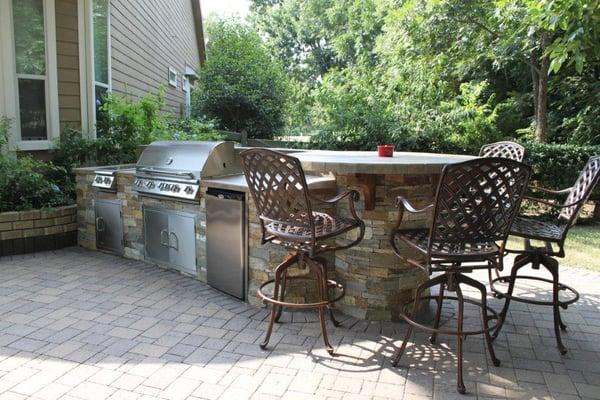 Custom outdoor kitchen with ledgestone exterior and circular table on one end, and a paver patio.