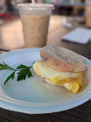 Egg and Cheese sandwich on an English muffin with Iced latte in the back