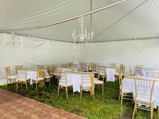 Tent package with 20x40 high peak frame tent, chandelier lighting, gold Chiavari chairs with white cushions, round tables and 12x12 floor