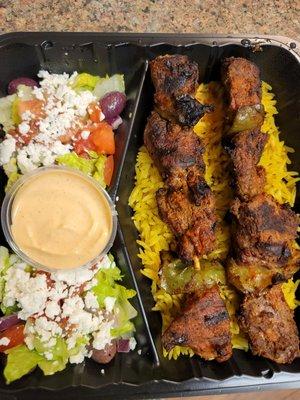 Lamb kebab plate with Greek salad and spicy sauce.