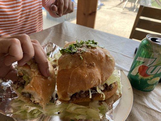 Torta with carne asada, loaded with lettuce, tomatoes, avocado and melted cheese over top.