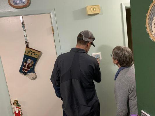 Technician, Kevin, shows furnace winner, Colleen, how to use her new thermostat