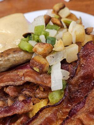 Close-up of bacon, scrambled eggs, sausage, homefries, and a yeast roll.