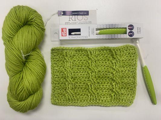 Malabrigo Rios Yarn in the color Apple Green. Coordinating Prym Crochet Hook and sample of crocheted fabric using crochet cables pattern.