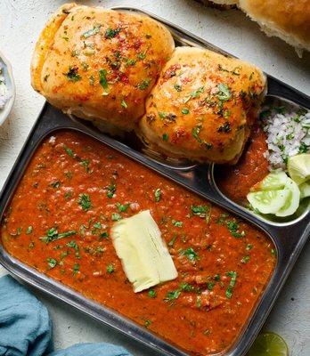 Pav Bhaji features a rich and flavorful vegetable curry made with mashed potatoes, tomatoes, peas, carrot, and a blend of aromatic spices.