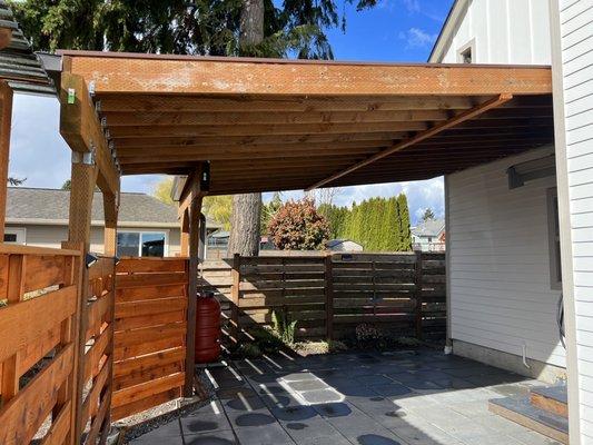 Carport with metal roof, pavers, rain barrel.