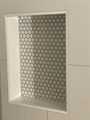 The niche that is located on the wall opposite the shower head.