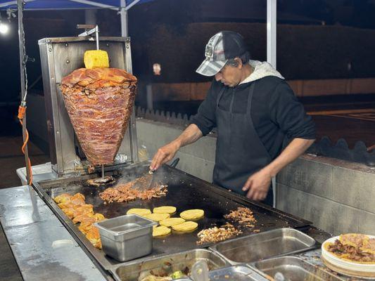 Tacos being prepared, al pastor and chicken and carne asada in the photo