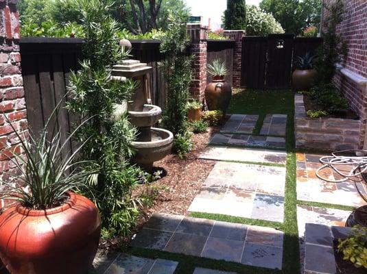 Side yard patio with synthetic turf, fountain, and stone paito