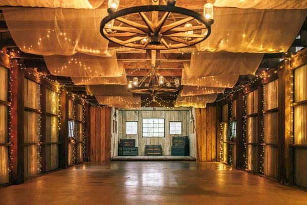 The rustic charm of this barn, accentuated by warm string lights and elegant drapes, offers a cozy and customizable venue for a wedding.