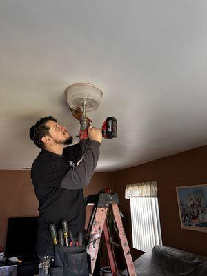 Louie precisely cutting ceiling plaster for recessed LED light in living room.