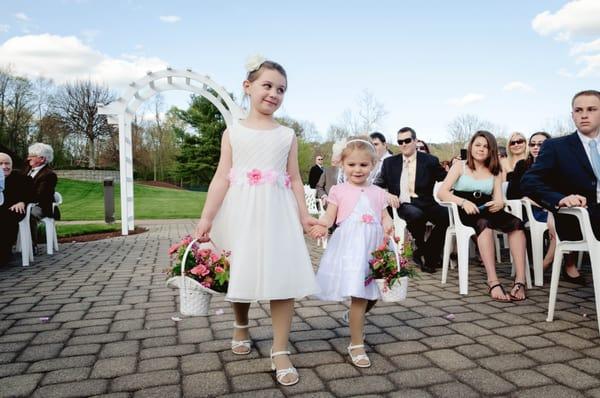 Leise Jones Photography; Two flower girls walk down the aisle during an outdoor wedding ceremony.