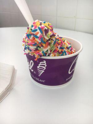 A small cup of soft serve vanilla ice cream with rainbow sprinkles.