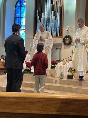 Presentation of the gifts during mass. Father Alphonse on the left with Deacon David on the right to receive the gifts from the alter