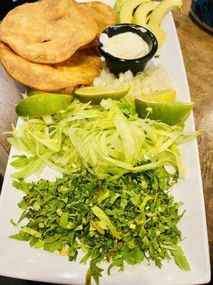 Side dish with the add in for the Carnitas Pozole. Cilantro, onions, sour cream, limes, avocado and tostadas.