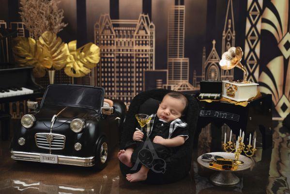 Newborn Luxury photography. Baby holding a glass wearing a suit with black elegant car in background.