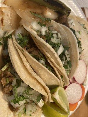 Steak tacos with cilantro and onions on double corn tortillas. Side: Lime wedges, radishes, carrots, onion slices and a roasted jalapeño.