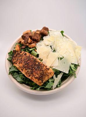 A bed of kale with shaved parmesan cheese, croutons, FG signature jerk salmon and jerk caesar dressing