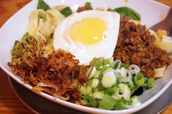 Curry Lamb Pan Mee: pan mee noodles, minced lamb dry-curry, spinach, shallots, green onions, anchovies, toasted coconut, fried egg ($15.95).