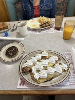 The three Crepe breakfast with a side of sausage patty in the foreground, while the 2 egg breakfast with a side of sausage links in the back