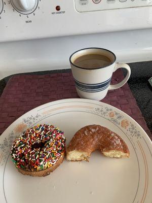 Frosted Cake Donut with Rainbow Sprinkles and half of Glazed Round Donut. Hot Coffee.