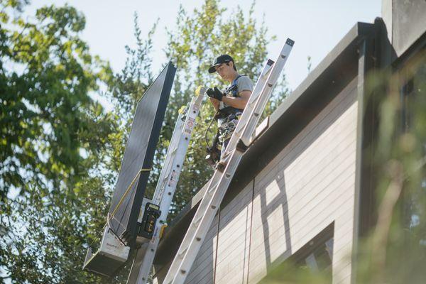 Using a ladder lift to safely hoist solar panels up three stories to the roof.