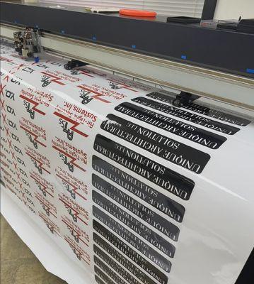 This image showcases our professional printing setup, featuring a wide-format vinyl plotter actively working on a roll of printed material.