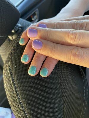 Kiddo hand with teal and sparkly gel manicure, adult hand with purple gel manicure.