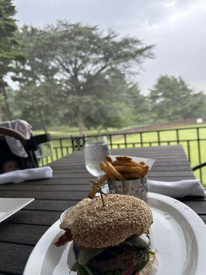 Bacon cheese burger with fries from their Specialty menu with background of the golf course