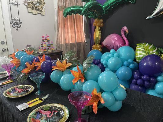 A view of the beautiful blue and orange colors for a Tropical tablescape and a photo booth backdrop with a fun pink flamingo vibe.