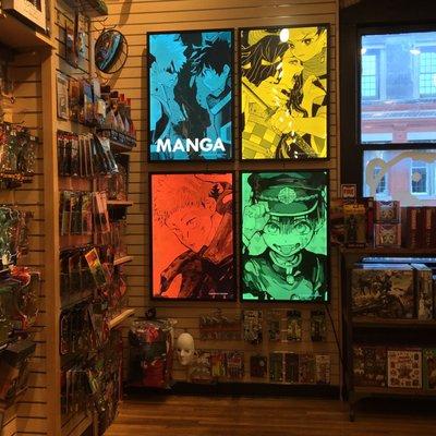 Four neon signs from different manga series. Surrounding the signs are items that are sold in the upstairs section in the store.