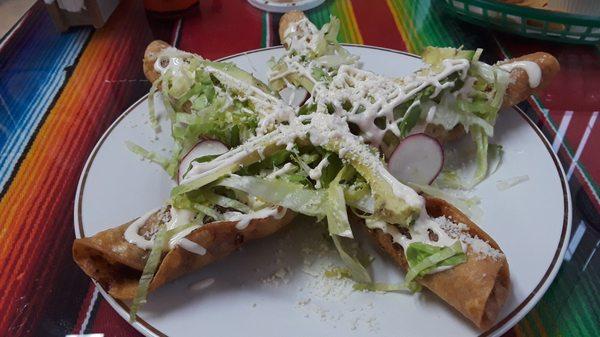 Flautas de Tinga de Pollo: Spicy shredded chicken wrapped in crispy tacos, topped w/ lettuce, radish, añejo cheese, avocado, & crema