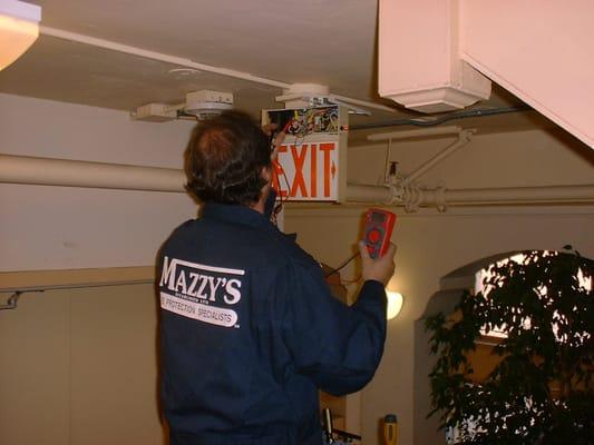 Mazzy's Fire Protection employee servicing an emergency exit light.