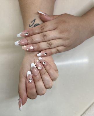 Elevating elegance with Gel X coffin nails adorned with pristine white French tips, embellished with diamond gems and intricate flowers.