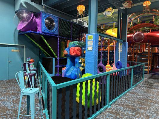 Toddler area that is fenced off to bigger children and contains crocheted swings, light features, slides, and safety flooring!