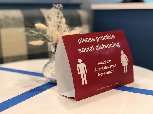 Social distancing sign is at each table with blue tape on them, indicating that no one should be sitting at those tables.