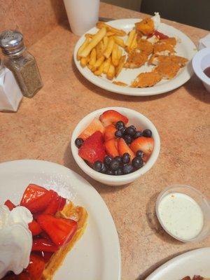 Side of fruit and a kids chicken strips and fries.