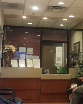 Width of the waiting room in the Endoscopy center. Receptionist hides behind glass and signs as you sit with a TV playing loud Ads