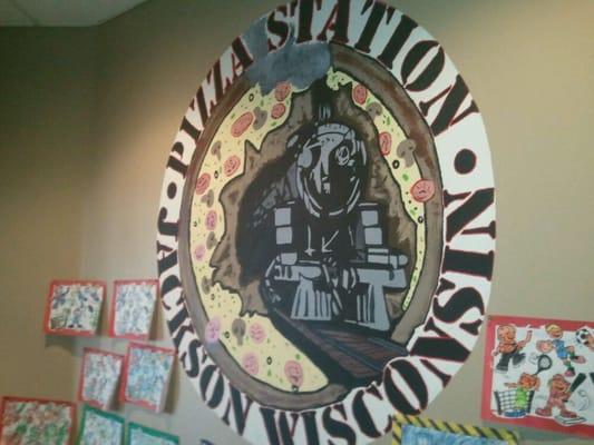 Painting on wall is a train coming out of a pizza. Restaurant has a train theme one of are employees painted the logo