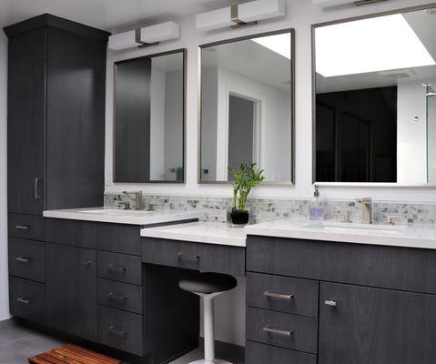 A modern luxurious bathroom featuring a custom configured vanity cabinet, built in makeup space, and tall linen cabinet.