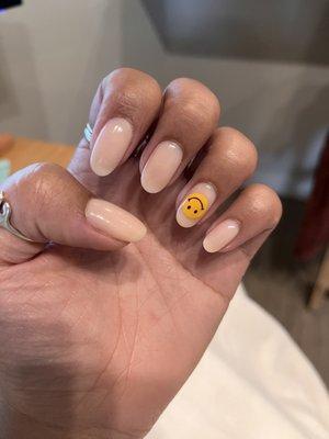 Neutral nails with yellow smiley face on ring finger.