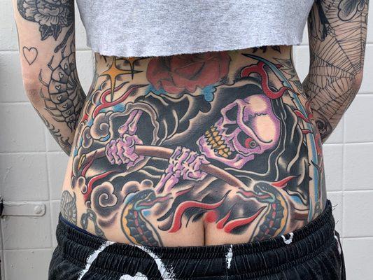 traditional american style tattoo of a grim ripper in a rad lower back by Kelley. His portfolio linked in our website. Book today!