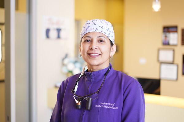 Dr. Munira Lokhandwala DDS with purple scrubs and a white surgical cap.